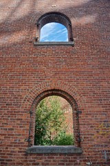 Brooklyn, New York, USA: Brick wall of an old factory with two windows showing the sky above and trees below.