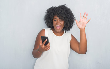 Young african american woman over grey grunge wall texting a message using smartphone very happy...
