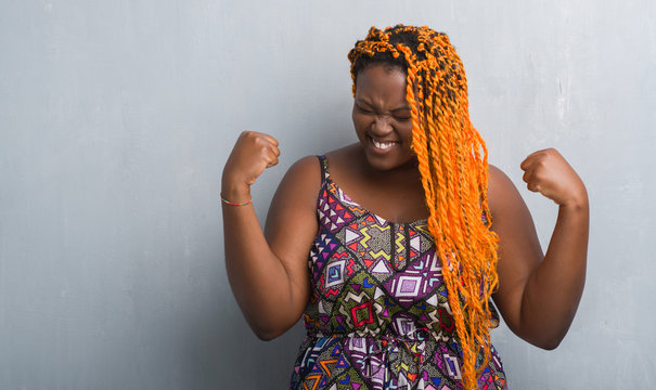 Young african american woman over grey grunge wall wearing orange braids very happy and excited doing winner gesture with arms raised, smiling and screaming for success. Celebration concept.
