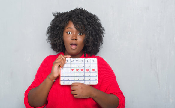 Young African American Woman Over Grey Grunge Wall Holding Menstruation Calendar Scared In Shock With A Surprise Face, Afraid And Excited With Fear Expression