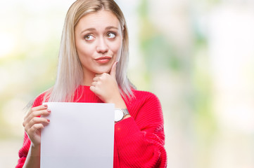 Young blonde woman holding blank paper sheet over isolated background serious face thinking about...