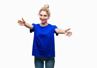 Young beautiful blonde and blue eyes woman wearing blue t-shirt over isolated background looking at the camera smiling with open arms for hug. Cheerful expression embracing happiness.