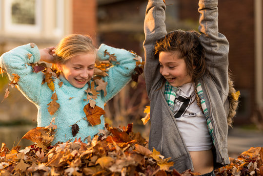 Girls having fun playing in a pile of autumn leaves