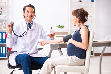 Obraz premium Young doctor checking pregnant woman's blood pressure