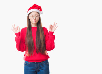 Obraz na płótnie Canvas Young Chinese woman over isolated background wearing christmas hat relax and smiling with eyes closed doing meditation gesture with fingers. Yoga concept.