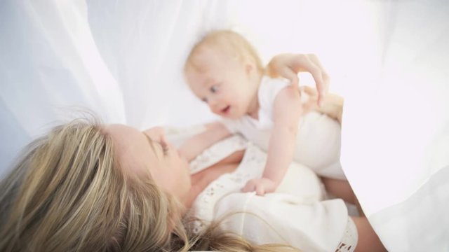 Attractive blonde young European mother relaxing with baby boy under white scarf outdoors 