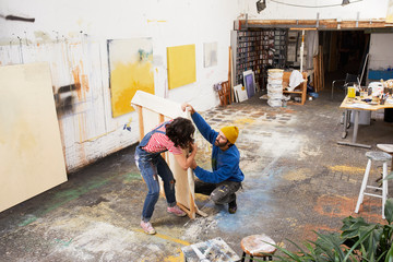 Female Artist Assisting Male In Stapling Canvas At Studio