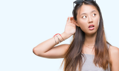 Fototapeta premium Young asian woman wearing sunglasses over isolated background smiling with hand over ear listening an hearing to rumor or gossip. Deafness concept.