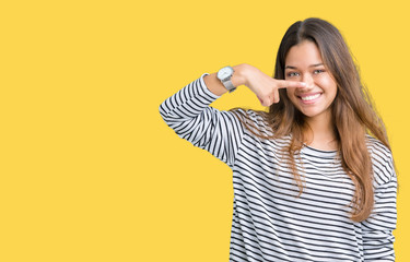 Young beautiful brunette woman wearing stripes sweater over isolated background Pointing with hand finger to face and nose, smiling cheerful