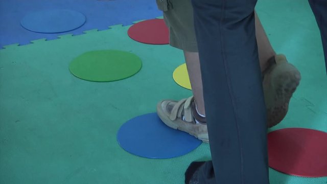 View of a disabled child's feet as an occupational therapist helps him walk on colored circles as they deal with a developmental disorder