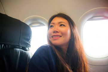 lifestyle candid portrait of young happy and beautiful Asian Chinese woman traveling for holidays inside airplane cabin excited on arrival smiling cheerful in tourist flight