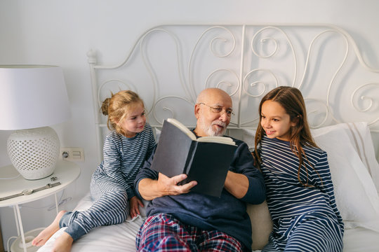Grandpa reading a book to their grandchild in the bed at morning. 