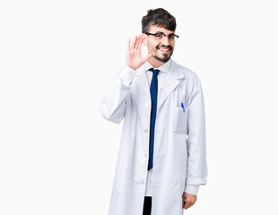 Young professional scientist man wearing white coat over isolated background smiling with hand over ear listening an hearing to rumor or gossip. Deafness concept.