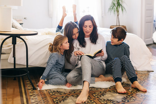 Mom and her kids reading a book at home in the morning. 