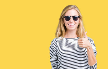 Fototapeta premium Beautiful young woman wearing sunglasses over isolated background doing happy thumbs up gesture with hand. Approving expression looking at the camera with showing success.