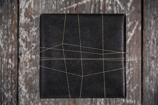 Gift wrapped in black with golden string on wooden surface