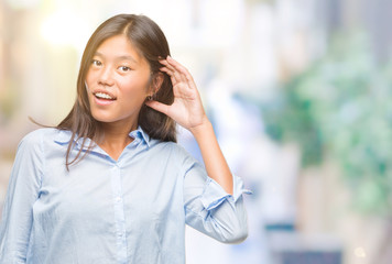 Young asian business woman over isolated background smiling with hand over ear listening an hearing to rumor or gossip. Deafness concept.