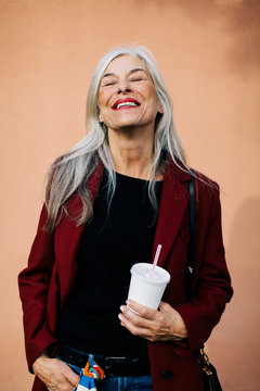 Portrait of mature woman with grey long hair holding a refreshment on the street.