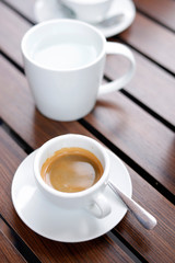 Espresso coffee hot in wooden black background, with spoon and warm water in white glass.