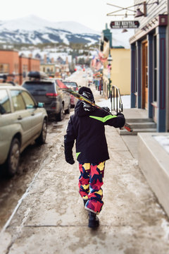 Child walking through ski town with skis on shoulder