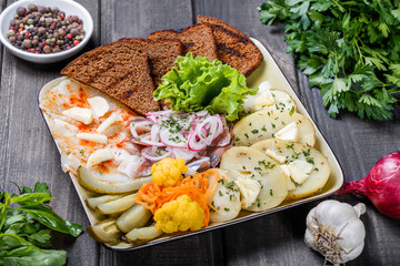 Appetizer platter, baked potato, delicious sliced pork fat with spices, sliced smoked fish with onions, pickles and bread on wooden background. Russian cuisine