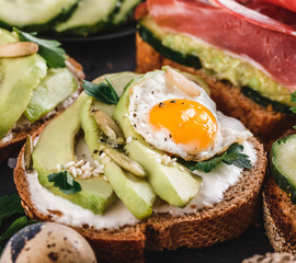 Whole grain bread sandwiches with fried quail egg, avocado, herbs and seeds on black background. Clean eating, healthy vegan breakfast