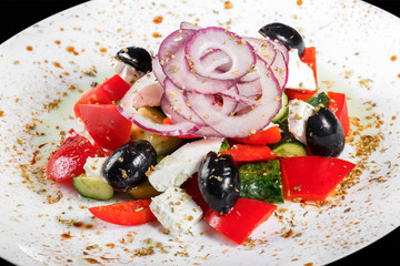 Greek salad with fresh vegetables, olives and feta cheese in plate, isolated on black background. Top view