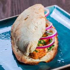 Grilled chicken in sandwich from fresh pita bread with onion and greens on dark wooden background....