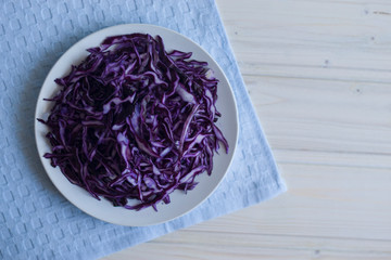 Photo salad of chopped purple cabbage in a plate on a blue napkin on a light background.