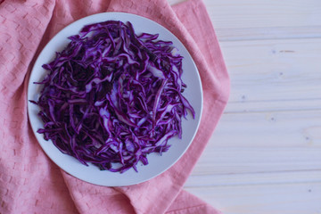 Photo salad of chopped purple cabbage in a plate on a pink napkin and a light wooden background.