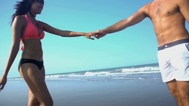 Happy smiling multi ethnic man and woman in swimsuits dancing barefoot on the sand on their beach holiday