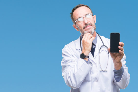 Middle age senior hoary doctor man showing smartphone screen over isolated background serious face thinking about question, very confused idea