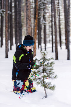 Boy in snow clothes decorating baby pine trees with lights