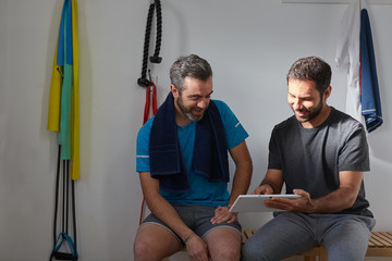 Sports coach and client friendly talking in the fitness club and sharing information from the digital tablet