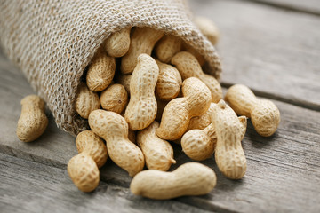 Peanuts in a miniature burlap bag on old, gray wooden surface