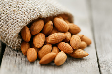 Almond nuts in a burlap bag on a wooden gray background.