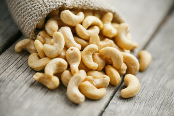 Cashew nuts in burlap bag on wooden gray background . Healthy food