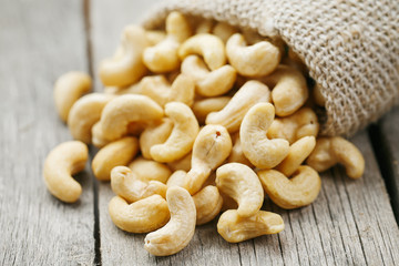 Cashew nuts in burlap bag on wooden gray background . Healthy food