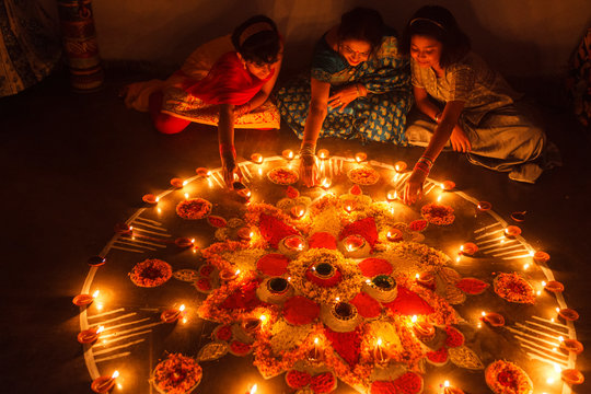 Woman and girls decorating rangoli and lighting Diya