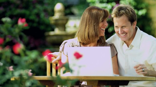 Young Caucasian couple at leisure using wireless technology in garden smiling and planning on laptop computer RED EPIC