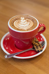 latte coffee with biscotti and latte art in red cup and saucer
