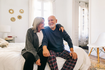 Portrait of elderly couple sitting on bed in the morning. 