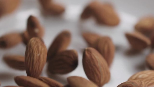 Slow motion closeup roasted almond falling in white bowl