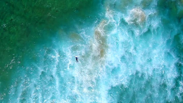 AERIAL: Birdseye view from 80 metres of surfer battling the waves, current and white wash in a turbulent ocean.