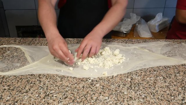 The cook sprinkles cheese and mint to the thin dough as he prepares a stuffed dough meal in the Middle East