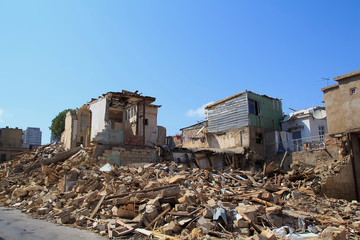 Disaster scene full of debris, dust and damaged house.