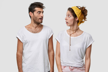 Suprised female and male discuss something unbelievable, look with widely opened eyes, have...