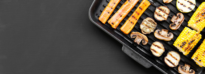 Grilled vegetables in a grilling pan over black background, overhead view. Space for text.