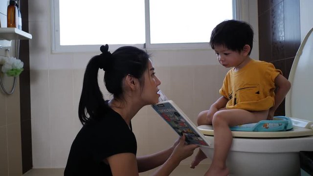 mother reading book with her son sitting on flush toilet