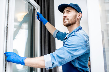 Man as a professional cleaner in blue uniform washing window with rubber brush indoors